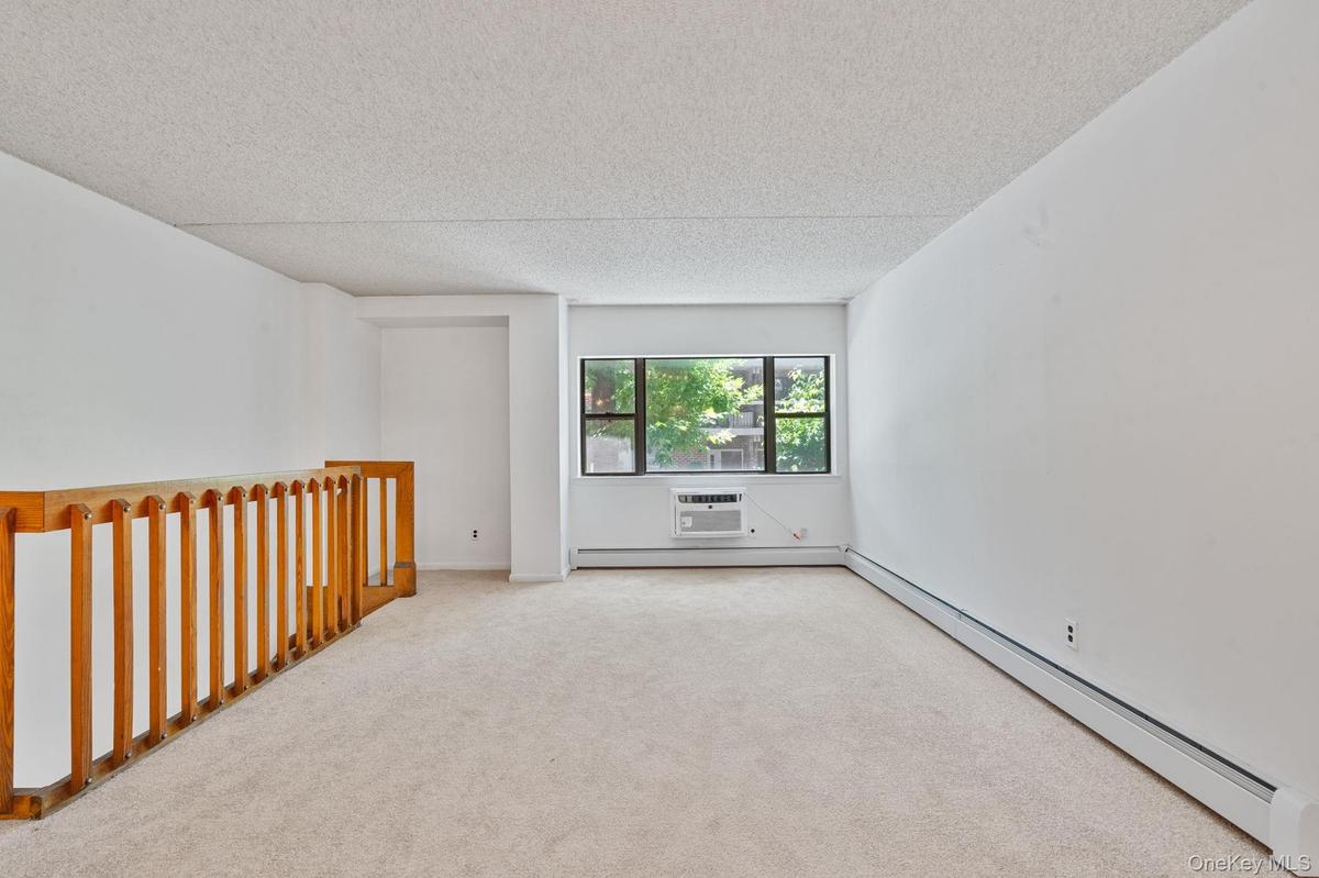Carpeted room featuring a window with exterior foliage, white walls, and a window-mounted air conditioning unit