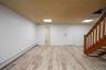 Spacious finished basement featuring wood-finish flooring, white walls, and a light-colored acoustical tile ceiling