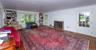 Spacious living area featuring expansive wood-finish flooring, a brick fireplace with a white mantel, built-in bookshelves flanking a large window, an