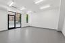 Spacious commercial interior featuring full-height storefront glass, a separate large window, recessed fluorescent lighting, light gray wood-finish fl