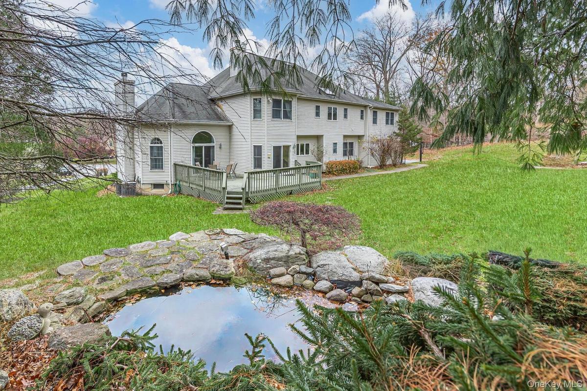 Rear view of property with a lawn, a chimney, a wooden deck, and a small pond