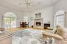 Living room with a stone fireplace, light wood-type flooring, ceiling fan, plenty of natural light, and a high ceiling