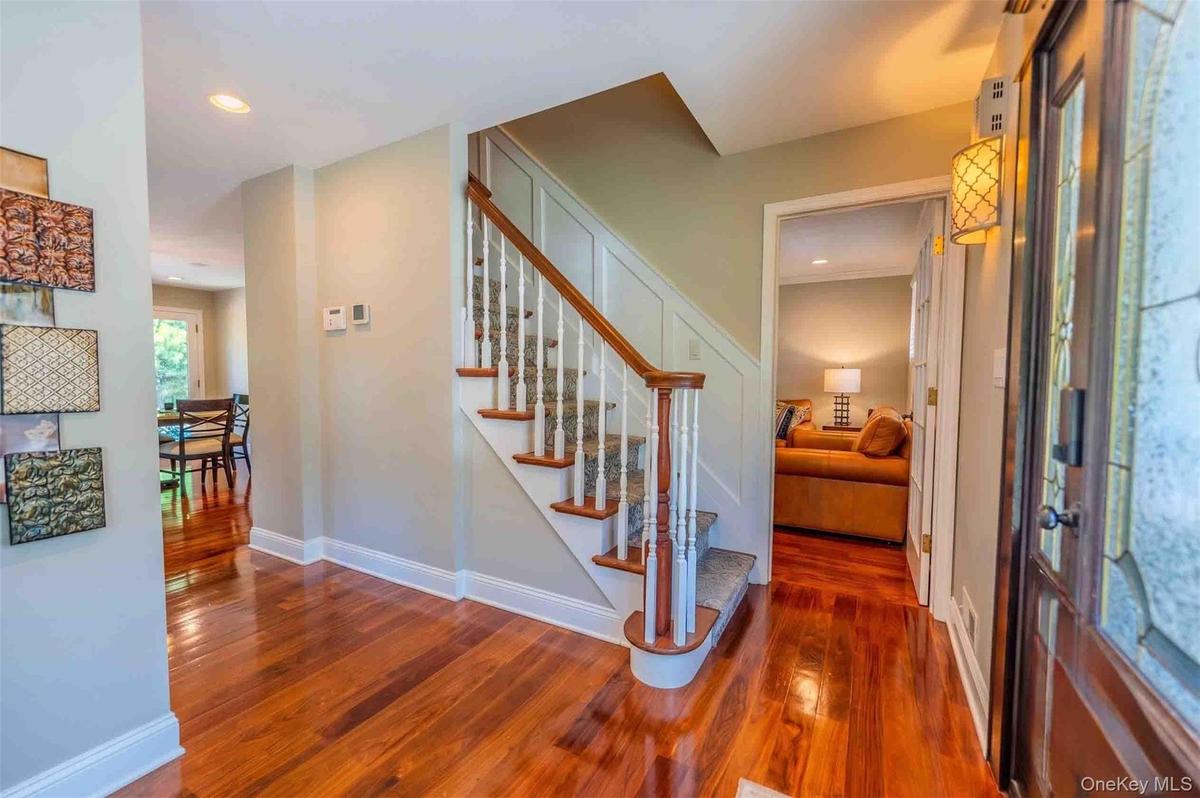 Warm and inviting entry foyer showcasing stunning gleaming hardwood floors, a beautiful wood-rail staircase, and an open layout that leads seamlessly 