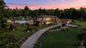 At dusk, the residence glows softly within its expansive grounds, where modern design meets a serene, estate-scale landscape