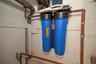 Dual whole-house water filtration system featuring blue filter housings and copper plumbing lines