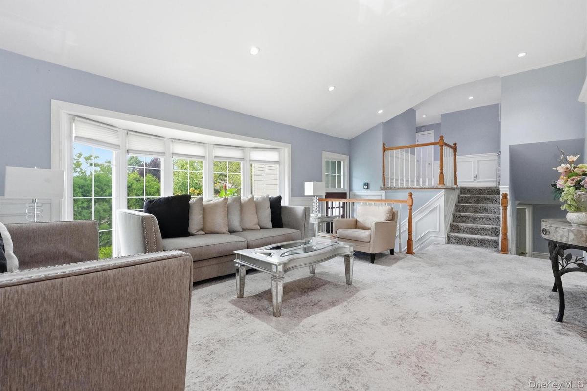 Spacious living area featuring a large bay window with outdoor views, recessed lighting, light-toned carpeting, and a staircase with wood railings