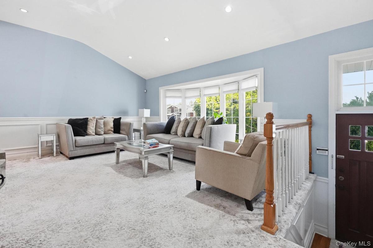 Living space featuring a vaulted ceiling with recessed lighting, light blue walls, and white wainscoting