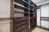 Custom closet system featuring dark wood-finish cabinetry, extensive shelving, integrated drawers with linear hardware, and multiple hanging rods