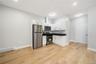 Open-concept living space featuring wood-finish flooring, white cabinetry, stainless steel appliances, and dark countertops