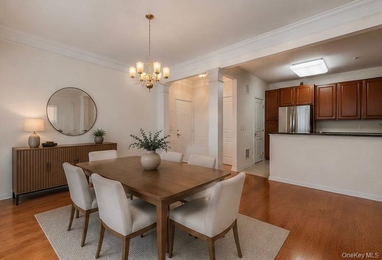 Open concept dining area featuring wood-finish flooring, a brass-tone chandelier, crown molding, and a partial view of the kitchen with dark wood cabi