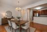 Open concept dining area featuring wood-finish flooring, a brass-tone chandelier, crown molding, and a partial view of the kitchen with dark wood cabi