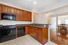 Kitchen featuring wood-finish cabinetry, black appliances including a gas range and built-in microwave, stone countertops, and tile flooring