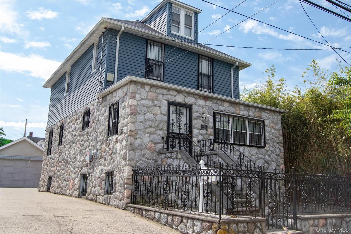 Stone and siding exterior with wrought iron railing, concrete stairs, and security bars