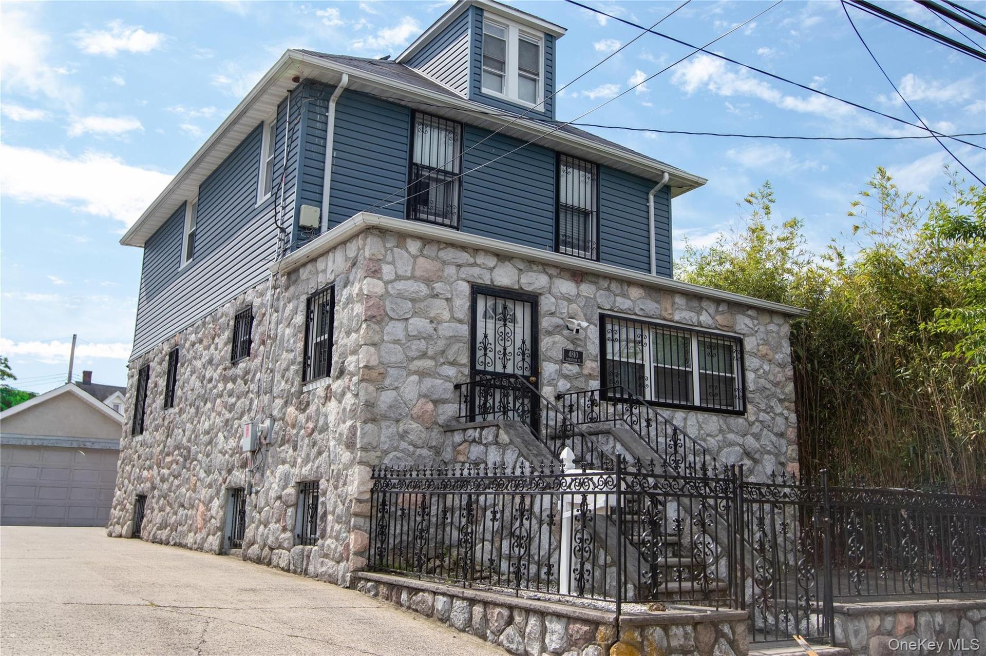 Stone and siding exterior with wrought iron railing, concrete stairs, and security bars