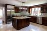 Kitchen featuring dark wood cabinetry, light granite countertops, stainless steel appliances, a center island with sink, and a tiled backsplash