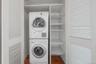 Dedicated laundry closet featuring a stacked washer and dryer, louvered bi-fold doors, integrated shelving, and hardwood flooring
