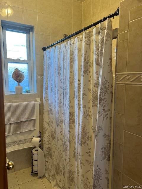 Tiled bathroom featuring a shower with a patterned fabric curtain, a framed window, and tiled walls