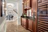 Bar area featuring wine cooler, ornamental molding, dark stone countertops, a raised ceiling, and glass insert cabinets