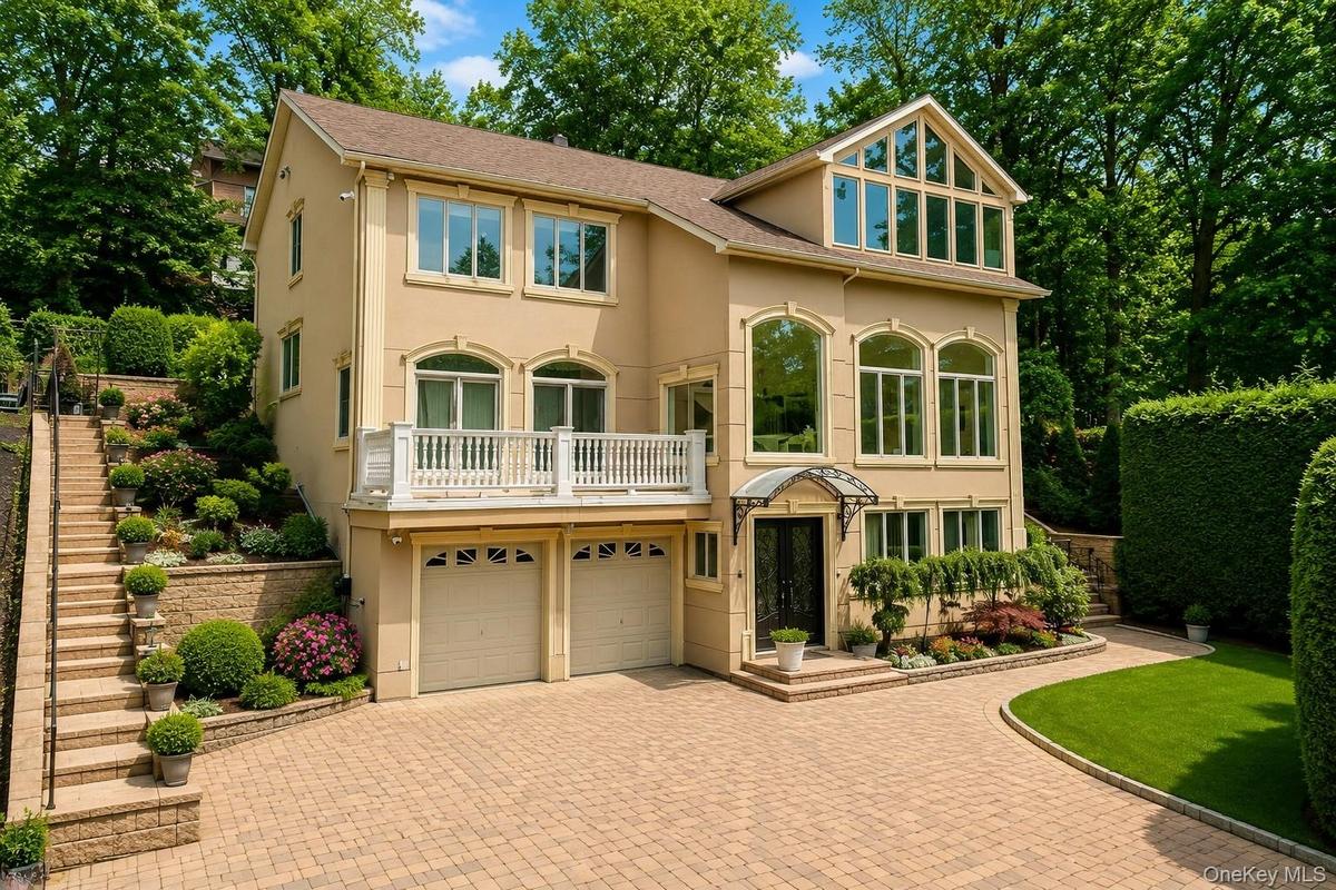 Stucco exterior with multiple arched windows, prominent balcony with white railing, and an expansive paved driveway