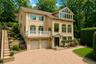 Stucco exterior with multiple arched windows, prominent balcony with white railing, and an expansive paved driveway