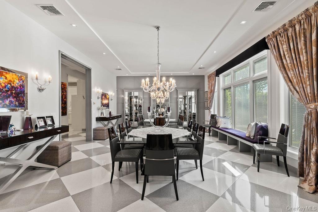 Spacious dining room featuring a large central chandelier, checkerboard tile flooring, a built-in window bench, and wall sconces