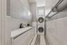 Dedicated utility area featuring a stacked washer and dryer, extensive countertop space, integrated sink, and upper cabinetry with textured paneling