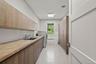Laundry room featuring extensive wood-finish cabinetry, a deep basin sink with a chrome faucet, light-toned countertop, and a window providing natural