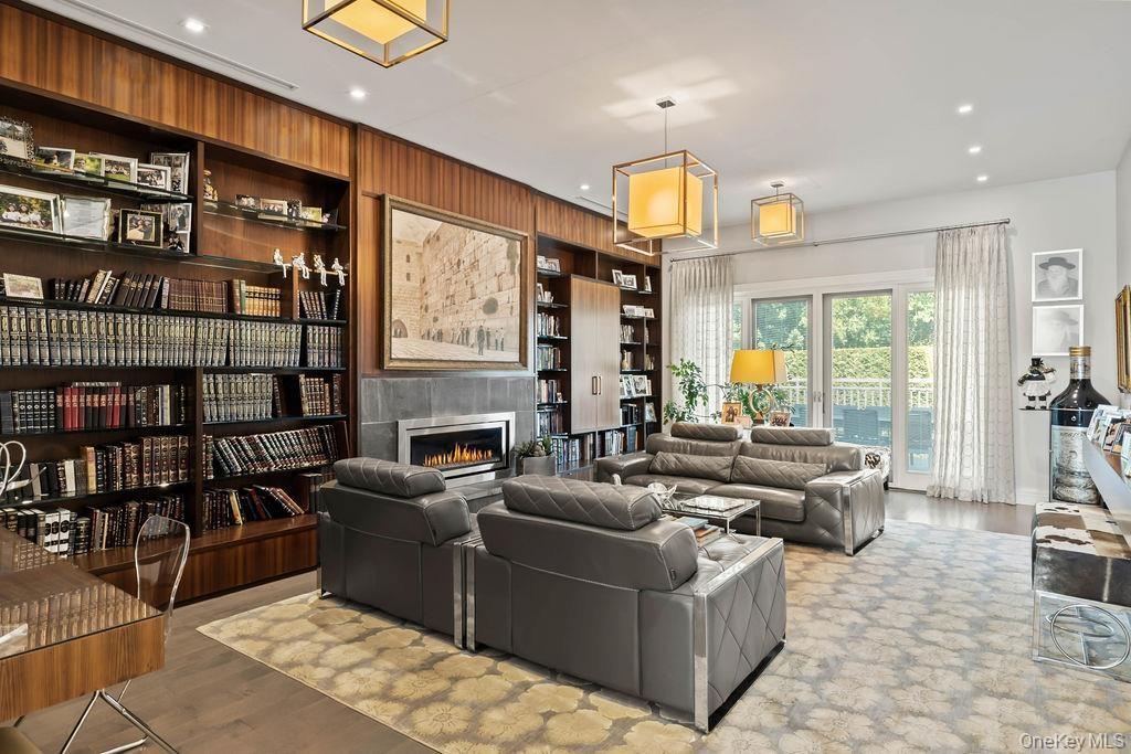 Wood-paneled library featuring extensive built-in shelving, a gas fireplace with a stone surround, recessed lighting, and elegant pendant light fixtur