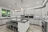 Modern kitchen featuring an expansive center island with an undermount sink, stainless steel appliances, light cabinetry, wood-finish flooring, and a 