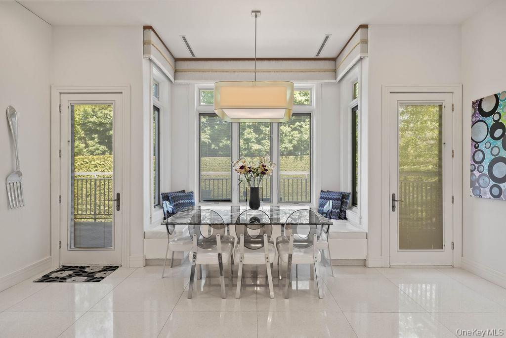 Bright dining area featuring a built-in window seat, large windows with garden railings, and two glass-paneled doors