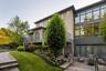 Rear stucco and stone veneer exterior featuring a large upper deck with metal railings, a full-height window wall, and a lower stone patio