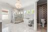 Spa-inspired, marble clad, primary bathroom featuring dual vanities, a soaking tub, a walk-in shower with dual shower heads, beautiful chandelier & Hu