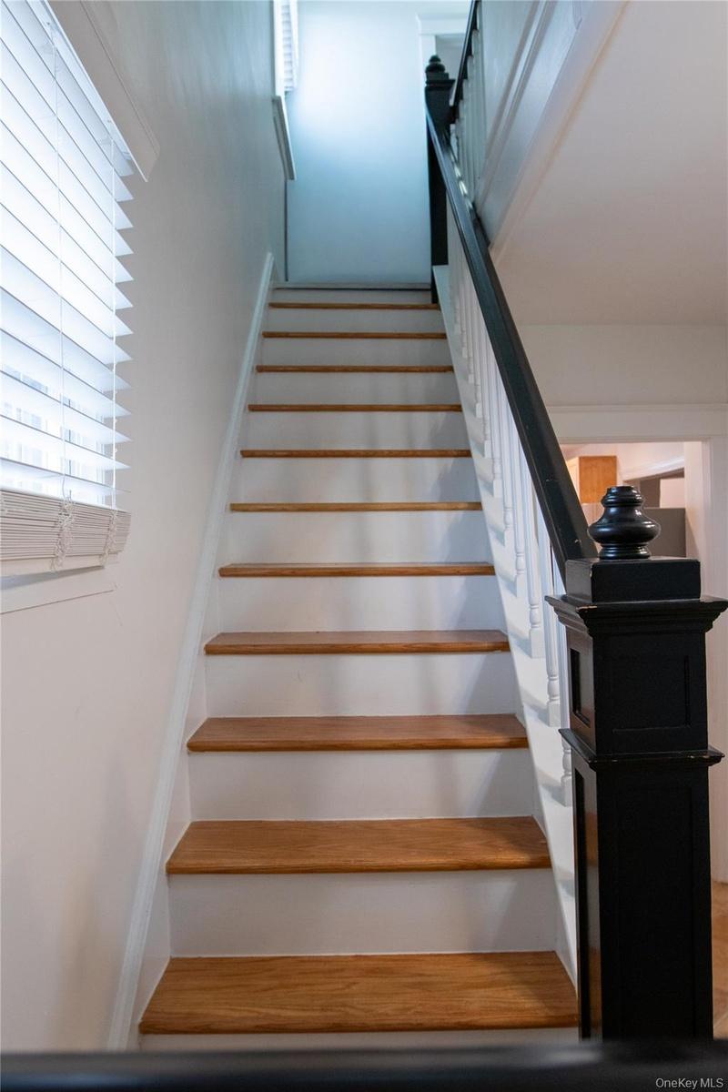Staircase featuring wood-finish treads, white risers, and a contrasting black newel post with a white spindle railing