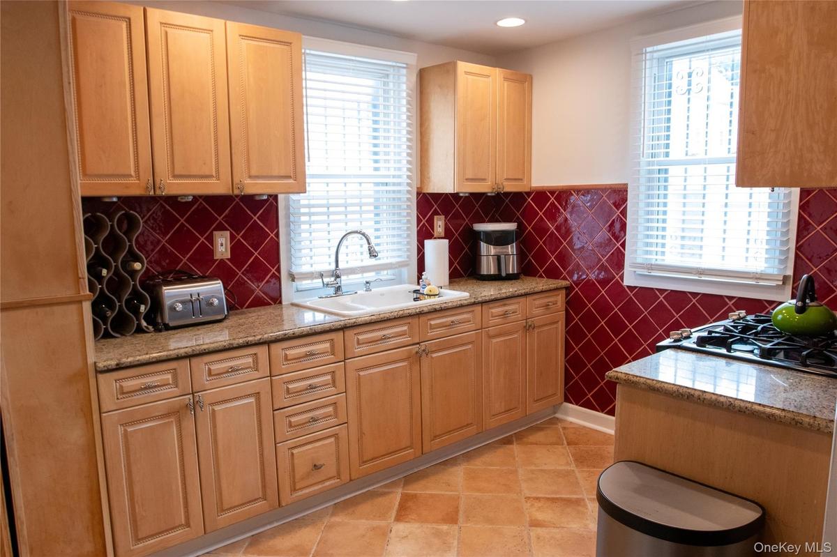 Kitchen featuring wood cabinetry, granite-finish countertops, and a red tiled backsplash