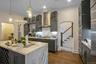 Kitchen with gray cabinetry, wall chimney exhaust hood, dark hardwood / wood-style flooring, an island with sink, and pendant lighting