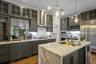 Kitchen featuring wall chimney exhaust hood, stainless steel appliances, light stone counters, an island with sink, and decorative light fixtures