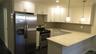 Contemporary kitchen featuring stainless steel appliances, white shaker cabinetry, a light-toned countertop, a subway tile backsplash, and dark wood-f