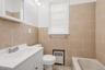 Bathroom featuring neutral-toned wall tiles, a white vanity with integrated sink, and a bathtub