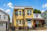 Yellow-sided multi-story residence featuring bay windows, a prominent white entry door, and a black wrought-iron fence
