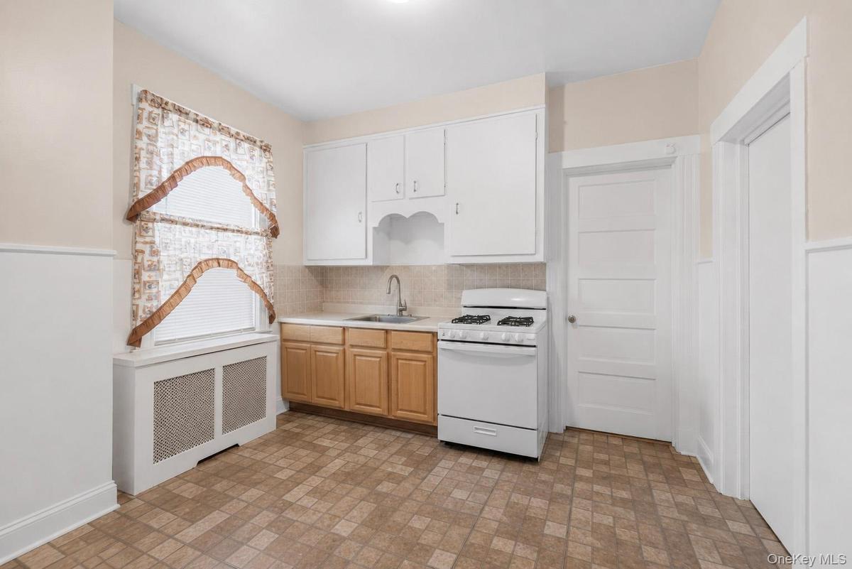 Compact kitchen with patterned floor tiles, white wainscoting, and built-in shelving