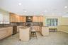 Spacious kitchen featuring light wood cabinetry, stone countertops, stainless steel appliances, and a central island with bar seating