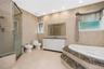 Spacious bathroom featuring a glass-enclosed shower, built-in soaking tub with stone surround, a white vanity with double sinks and stone countertop, 