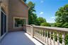 Outdoor balcony featuring light-toned flooring, ornate balusters, a large arch-top door, and a rectangular window with decorative trim