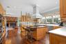 Kitchen featuring ornamental molding, dark wood finished floors, a fireplace, a center island, and glass insert cabinets