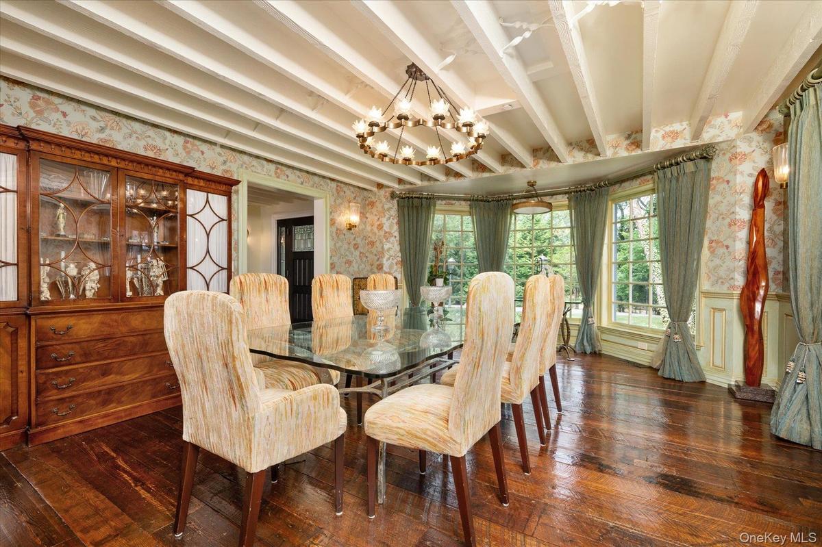 Dining area featuring wallpapered walls, a chandelier, hardwood / wood-style flooring, beam ceiling, and wainscoting