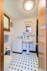Bathroom featuring a black and white tiled floor, a white pedestal sink, a white medicine cabinet, a white storage cabinet, and a window with blinds
