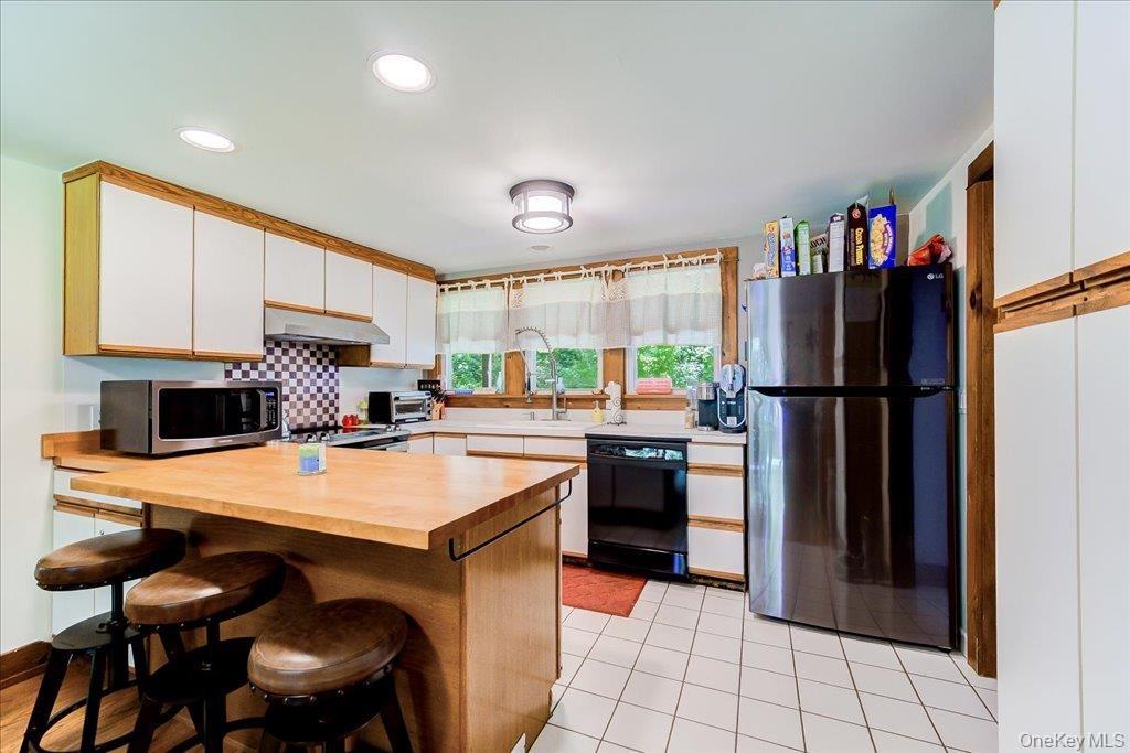 Kitchen featuring a wood-finish island with counter seating, white cabinetry with wood trim, white countertops, tile flooring, and a stainless steel r