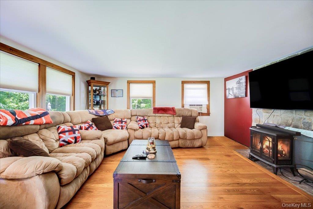 Living area featuring wood-finish flooring, multiple windows with natural wood trim, a stone-faced hearth, and a freestanding fireplace
