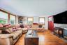 Living area featuring wood-finish flooring, multiple windows with natural wood trim, a stone-faced hearth, and a freestanding fireplace