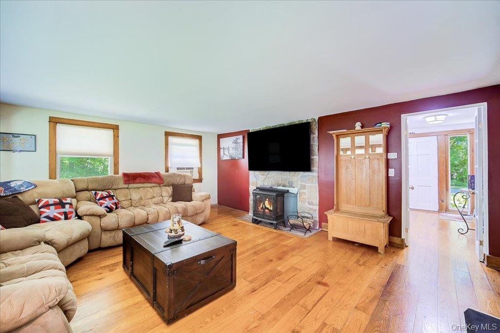 Living area featuring wood-finish flooring, a stone accent wall with a built-in wood stove, and natural wood trim around windows and doorways